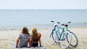 Two people sitting on a beach towel facing the sea, with a bicycle leaning against the sand. - Compass Rose Cottage ★ Steps to Flax Pond & Nature Trails ★ Kayaks  (Dennis)
