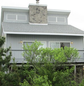 A two-story house with a stone chimney, white siding, and a green roof.