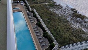 Vista de una playa desde un balcón, con piscina y sillas de descanso.