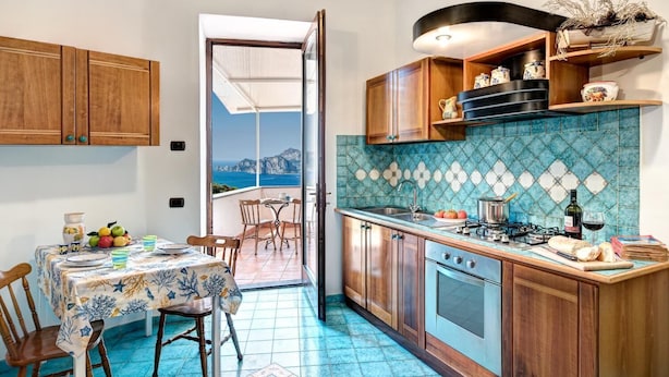 A kitchen with wooden cabinets, a tiled backsplash, and a dining area with a table set for two. - Campanella's Studios (Massa Lubrense)