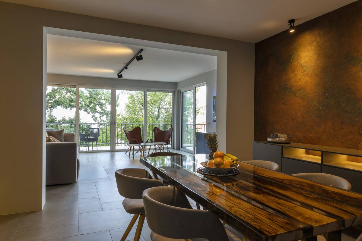 A modern dining area with a long wooden table, several chairs, and a fruit bowl.
