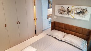A bedroom with a bed, a wardrobe, and a kitchen in the background.