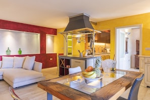A modern living room with a sofa, a glass dining table, and a kitchen area with a stove and cabinets. - Opatija Hills Ika - Luxury Apartments (Opatija)