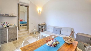 Un espacio habitable compacto con un sofá, una mesa de comedor con mantel azul, una pequeña cocina y una escalera visible que conduce a un nivel superior.