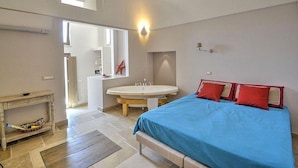 Un dormitorio con cama, mesita de noche, espejo y baño con lavamanos y espejo.