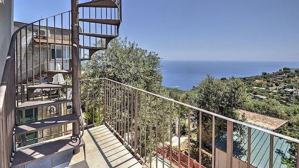 Un balcón al aire libre de varios niveles con vista al mar, una piscina y vegetación circundante.