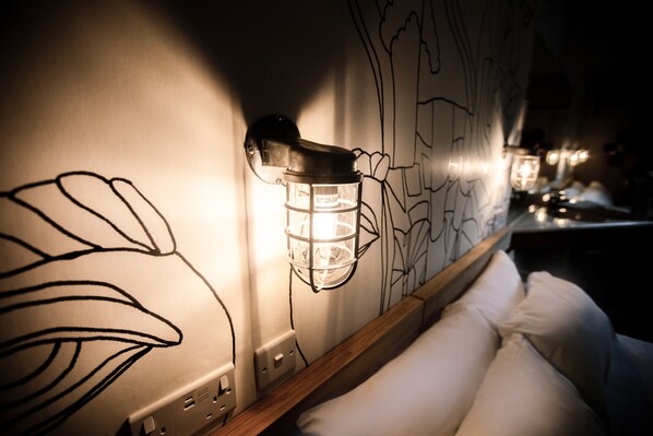 Pared con un dibujo lineal en negro de hojas y una lámpara fijada a la pared.