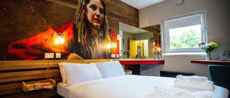 A hotel room with a large bed, a wooden headboard, a mirror, a window, and a wall with a mural.
