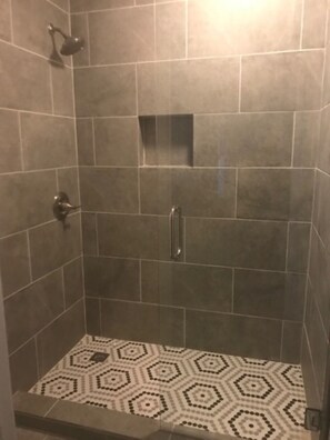 Ducha con un diseño geométrico de azulejos en el suelo y un pequeño azulejo cuadrado en la pared.