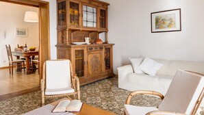 Ein Wohnzimmer mit einem weißen Sofa, einem Holzschrank und einem Esstisch mit Stühlen.