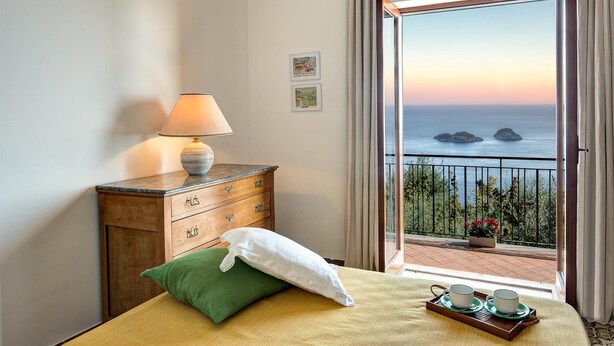 Ein Zimmer mit einem Bett, einem Holzschrank, einer Lampe und Meerblick vom Balkon.