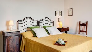 Ein ordentlich bezogenes Bett mit Kopfteil, zwei Nachttische mit Lampen, ein Holzstuhl und gerahmte Pflanzenbilder an der Wand.