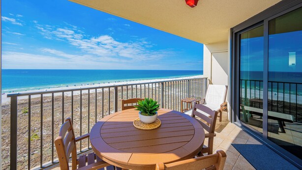 Een balkon met uitzicht op het strand, een tafel met stoelen en een plant in een pot.