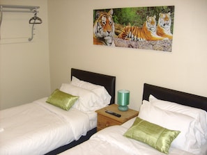 A hotel room with two single beds, white bedding, green pillows, a wooden nightstand with a remote control, and a painting of tigers on the wall. - Metro Inns Teesside (Stockton-on-Tees)