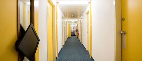 A hotel hallway with yellow doors, a blue carpet, and a fire extinguisher on the wall.