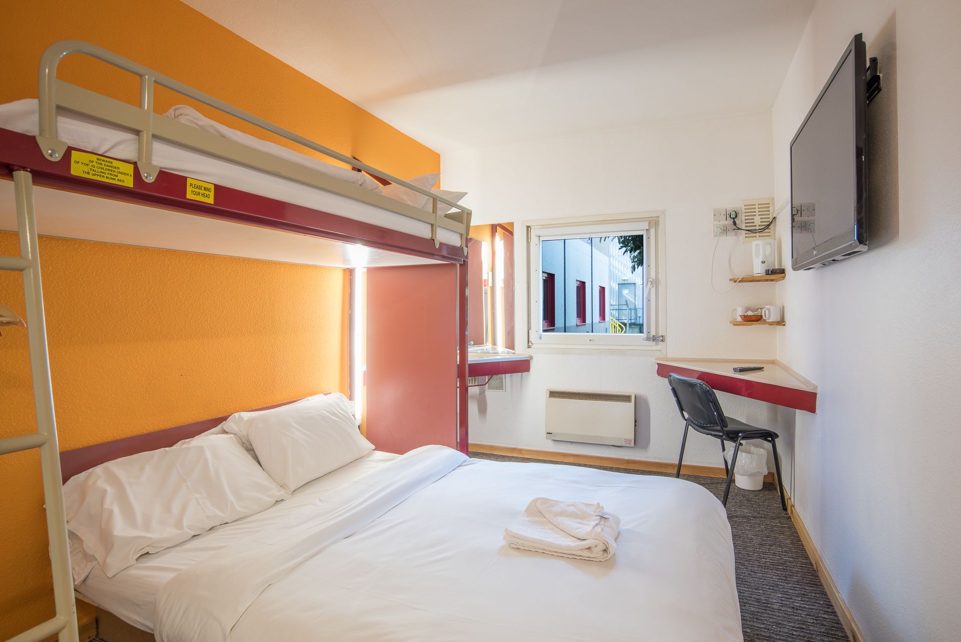 A bunk bed room with a desk, a chair, and a TV.