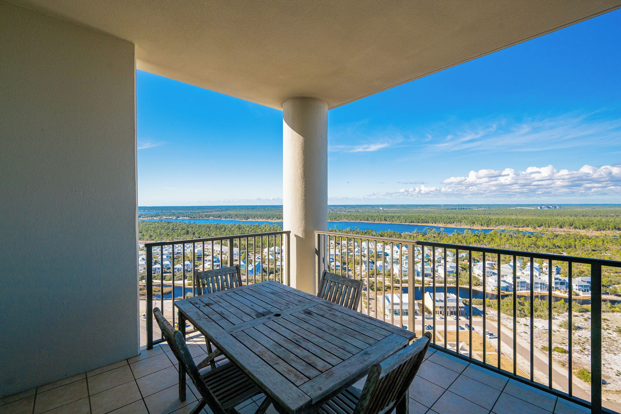 A balcony with a wooden table and chairs, offering a view of a lake and surrounding buildings.