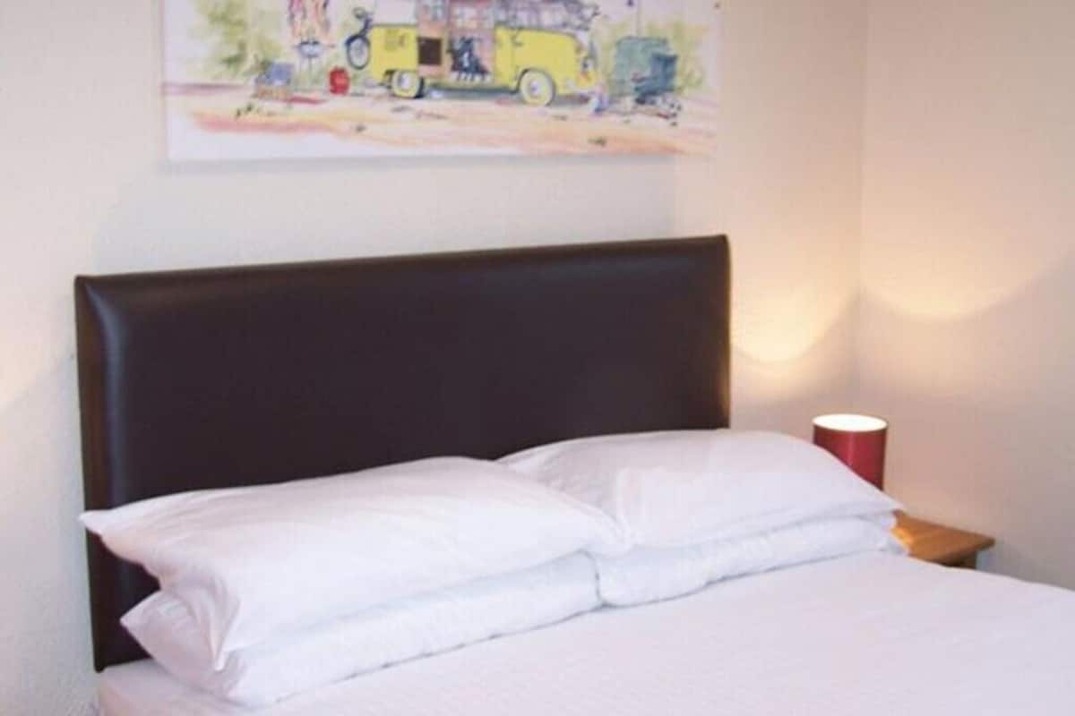 A neatly made bed with white linens in a room with a dark headboard.
