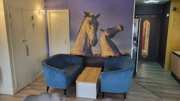 Ein modernes Wohnzimmer mit einem blauen Sofa, einem Holztisch und einem Wandgemälde von Pferden.
