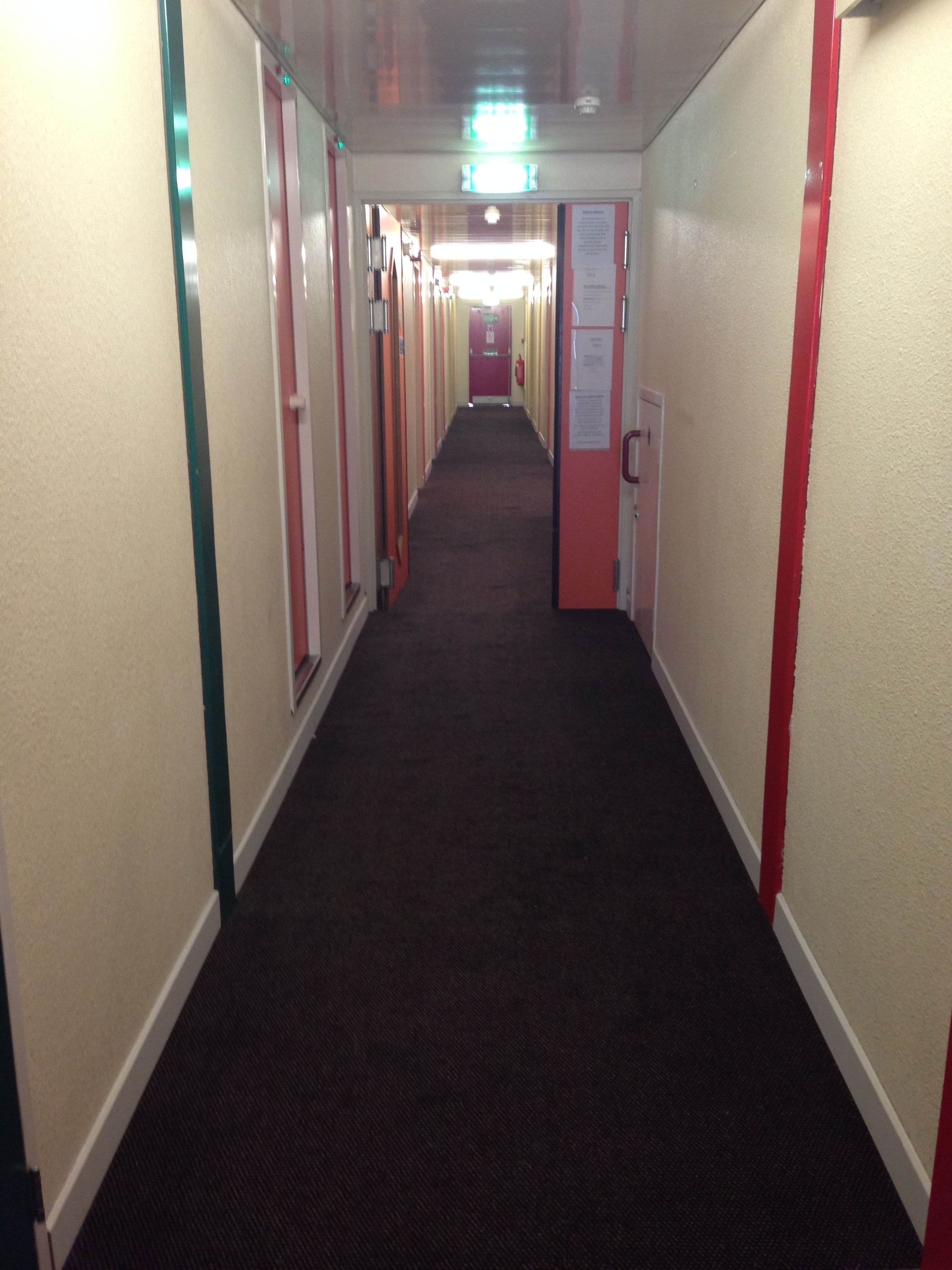 Een hotelgang met tapijtvloeren, deuren aan beide kanten en een plafondlamp.