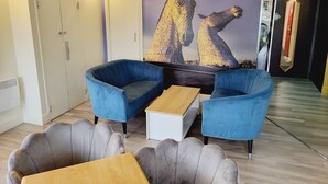 Ein modernes Zimmer mit zwei blauen Sesseln, einem grauen Sofa, einem Holztisch und einem Wandgemälde von zwei Personen.