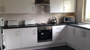A kitchen with white cabinets, a stove, a microwave, and a kettle.