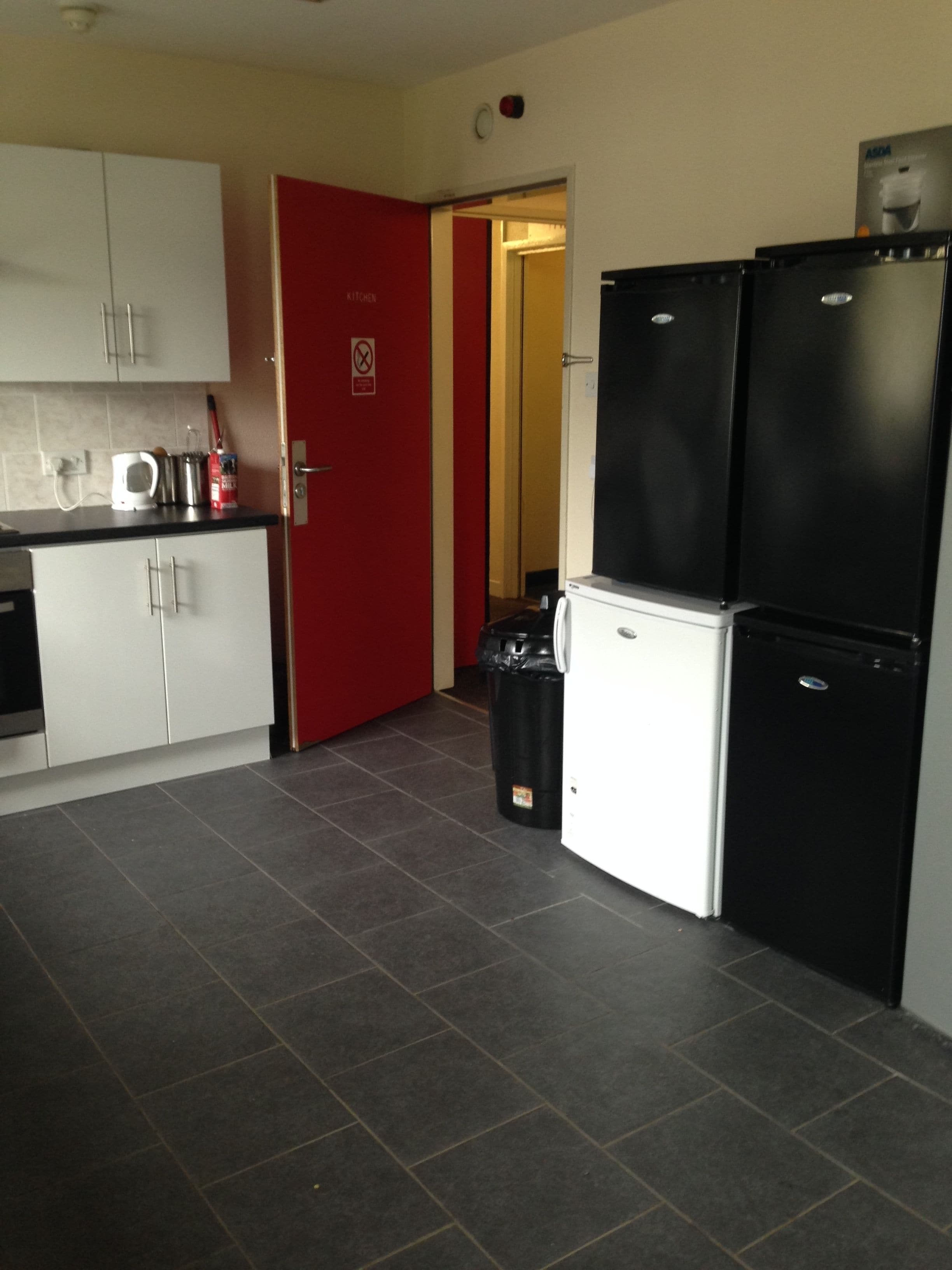 A compact kitchen with white cabinets, a red door, and a black refrigerator.