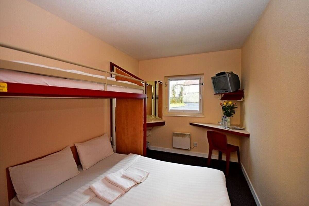 A compact hotel room with a bunk bed, a desk with a chair, a television, and a window.