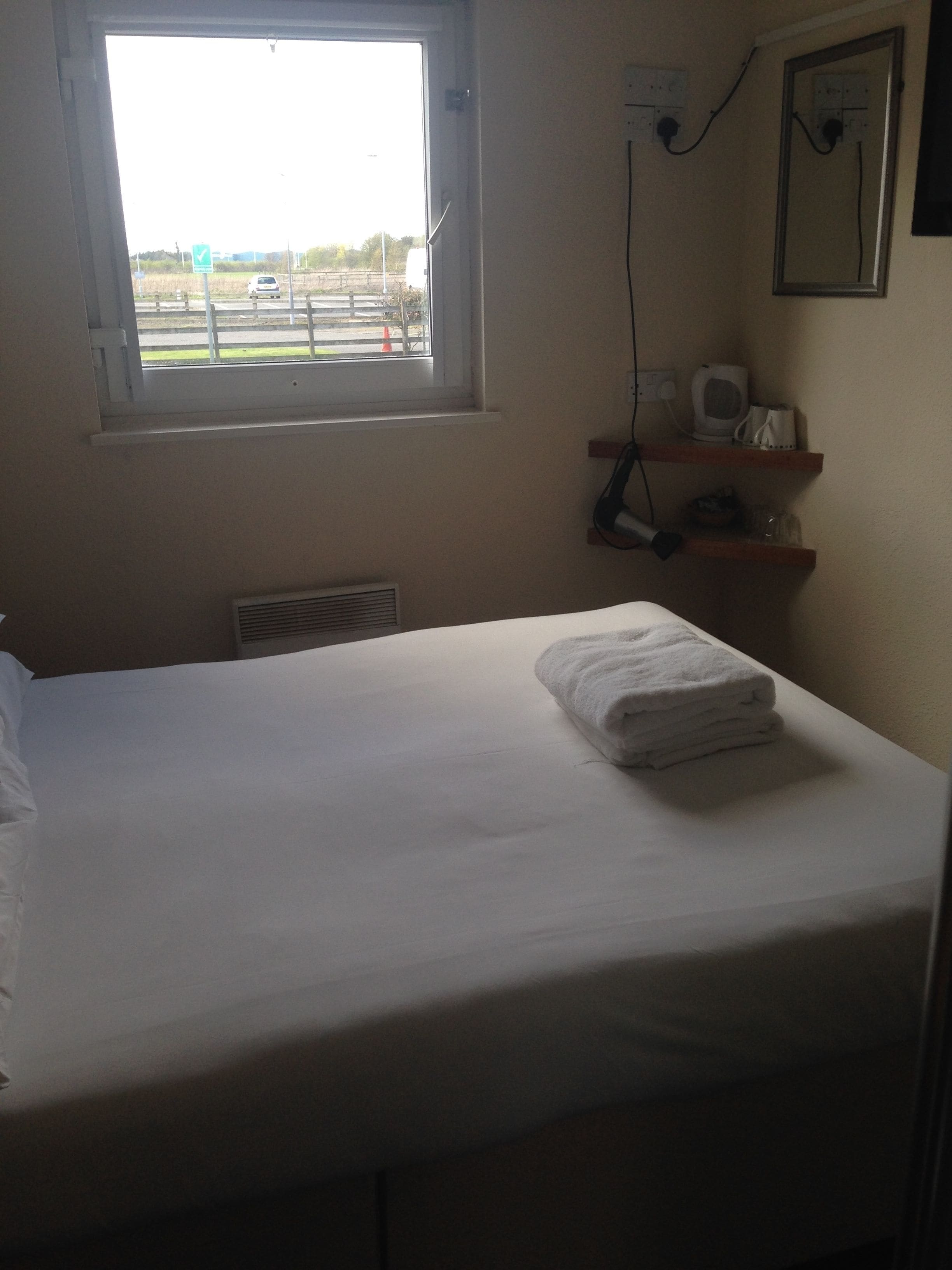 Habitación de hotel con cama, ventana, repisa con hervidor y teléfono, y toma de corriente.