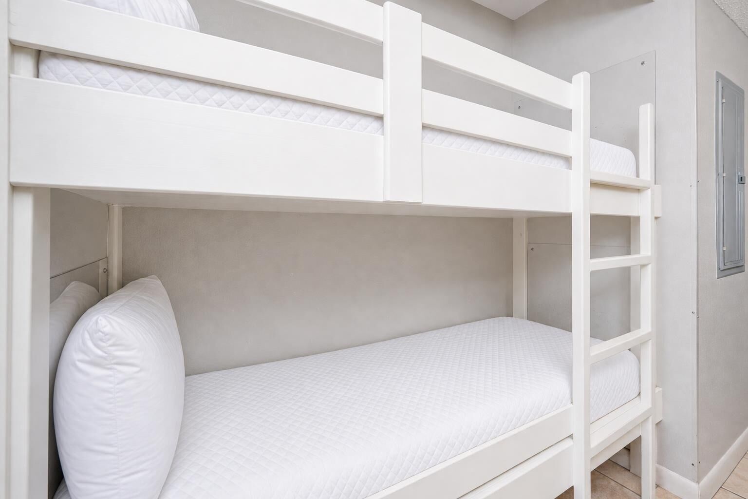 A bunk bed with white bedding and a ladder, a door, and a window with a view of the outside.