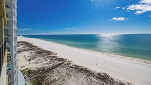 A beach with clear blue water, a white sandy shore, and a high-rise building in the background.