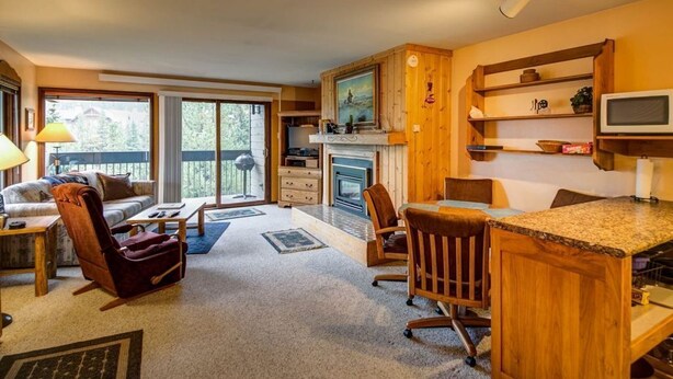A cozy living room with a fireplace, wooden furniture, and a large window.