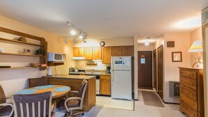 A compact kitchen with wooden cabinets, a microwave, a refrigerator, and a dining area with a table and chairs.