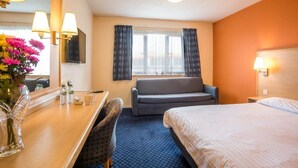 Una camera d'albergo con un letto, una scrivania con una sedia, un divano, una TV fissata al muro e una finestra con tende.