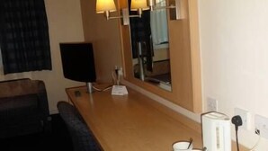 Camera d'albergo con una scrivania in legno, forno a microonde, macchina del caffè, uno specchio e una televisione.