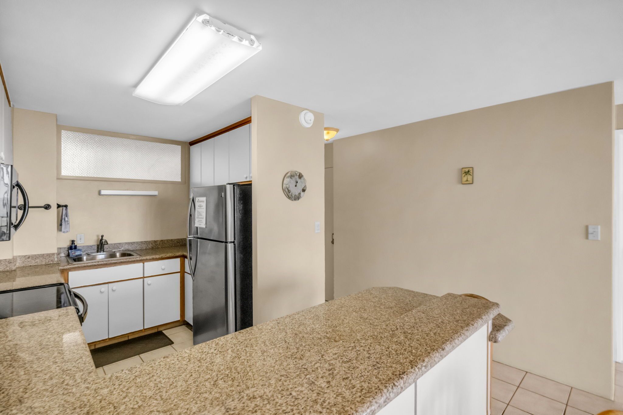 Una cocina con encimeras de granito, refrigerador de acero inoxidable y armarios blancos.