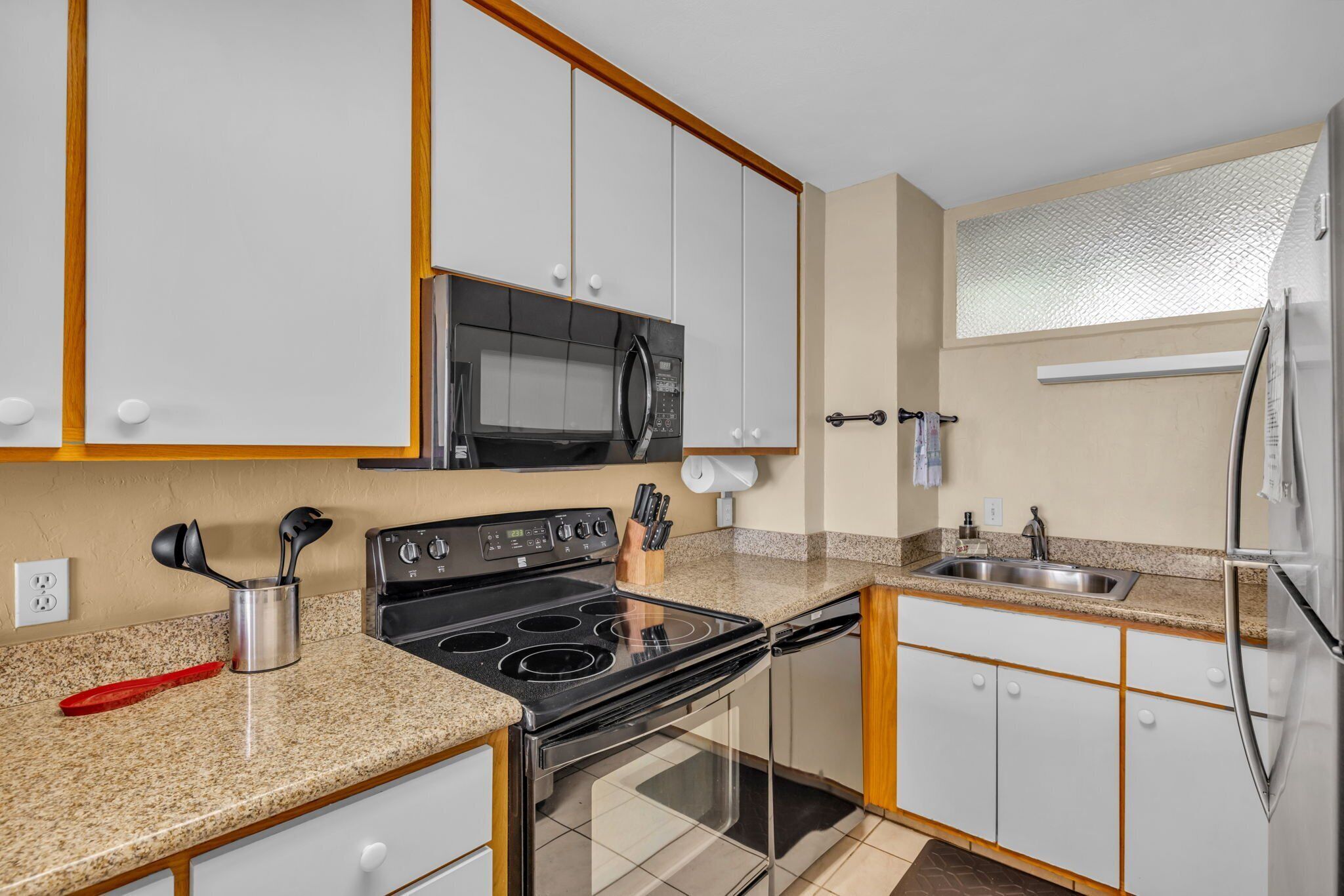 A modern kitchen with white cabinets, a stainless steel refrigerator, a microwave, and a stove.