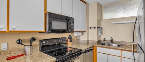 A modern kitchen with white cabinets, a stainless steel refrigerator, a microwave, and a stove.