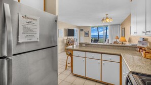Eine moderne Küche mit einem Edelstahl-Kühlschrank, einer Granitarbeitsplatte und Meerblick durch große Fenster.