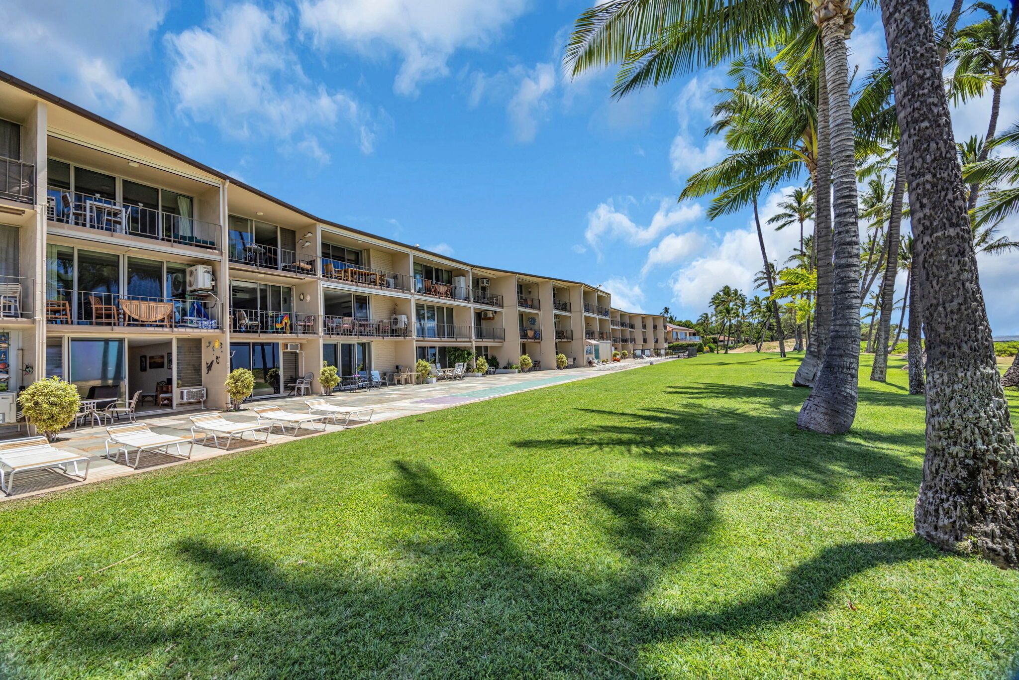 A multi-story hotel with balconies, a swimming pool, and palm trees.