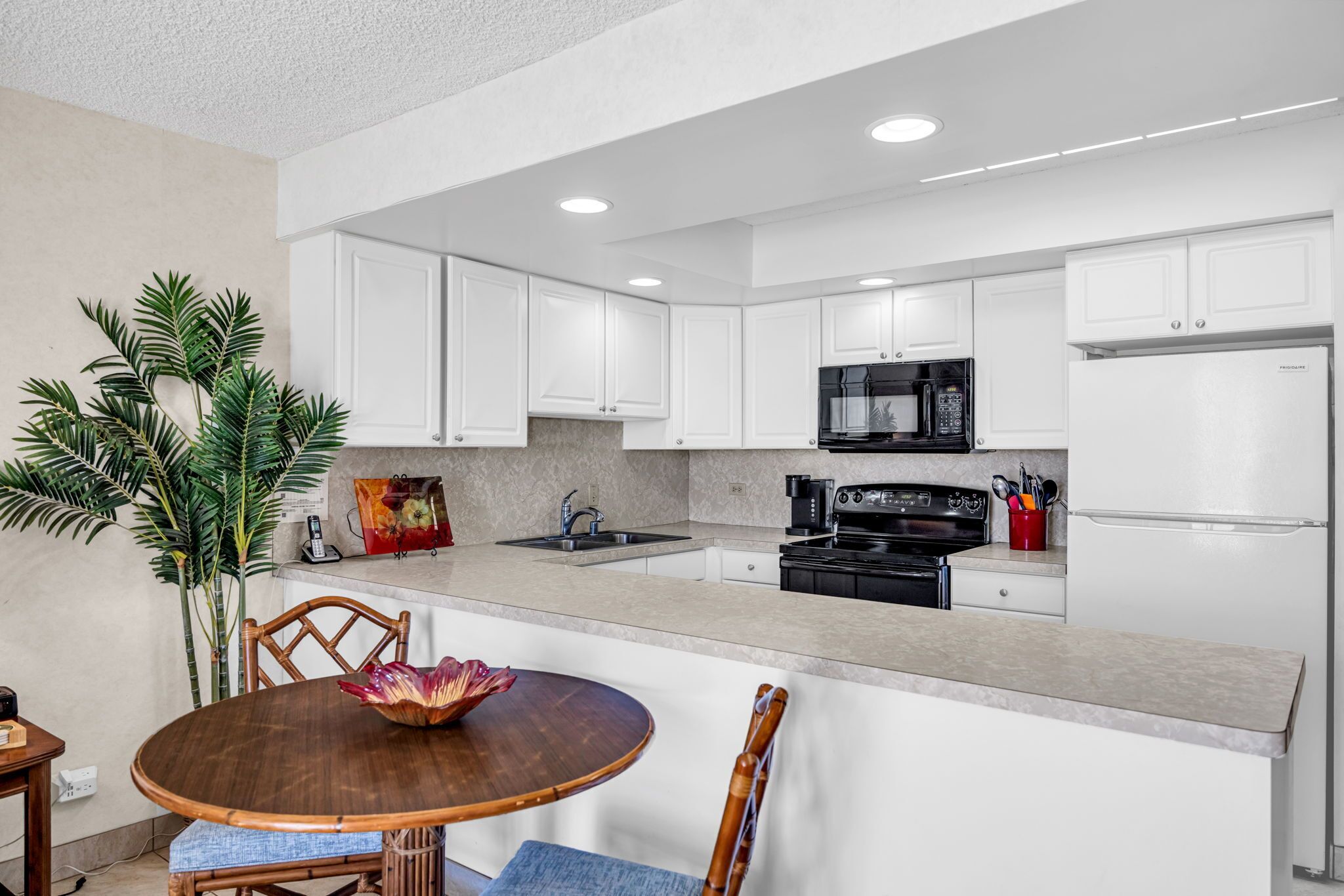 A modern kitchen with white cabinets, a central island, and a dining area with a wooden table and chairs.