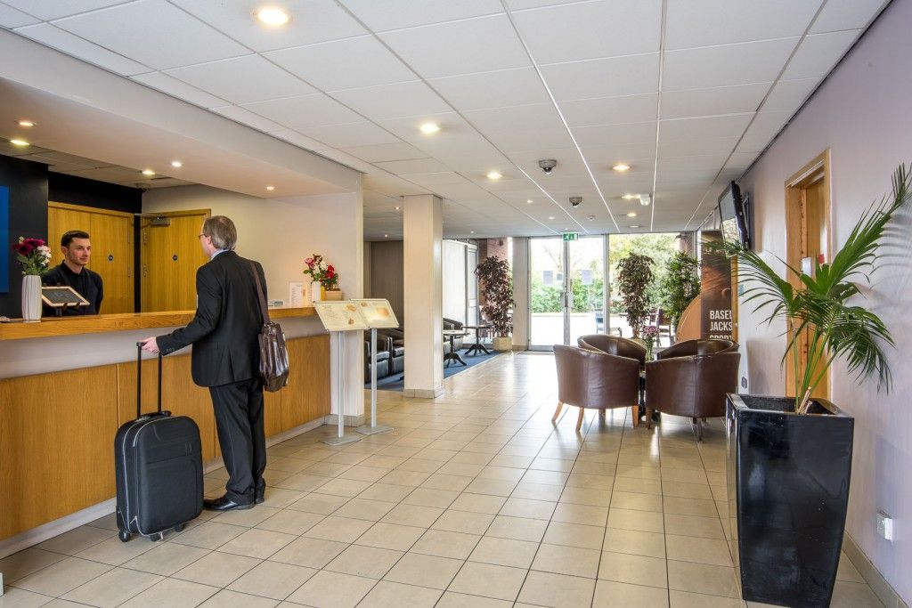 A hotel reception area with a reception desk, a man with a suitcase, and a sign for 'BASEL JACKS'.