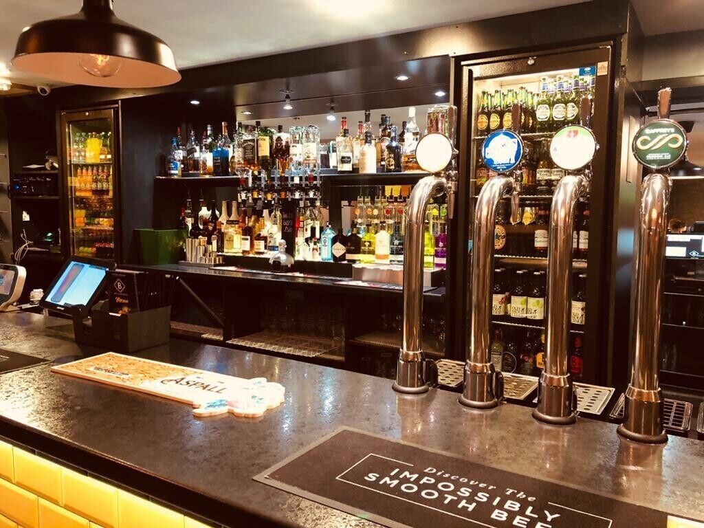 Zona de bar con múltiples grifos, un terminal de pago digital y una variedad de botellas de licor.