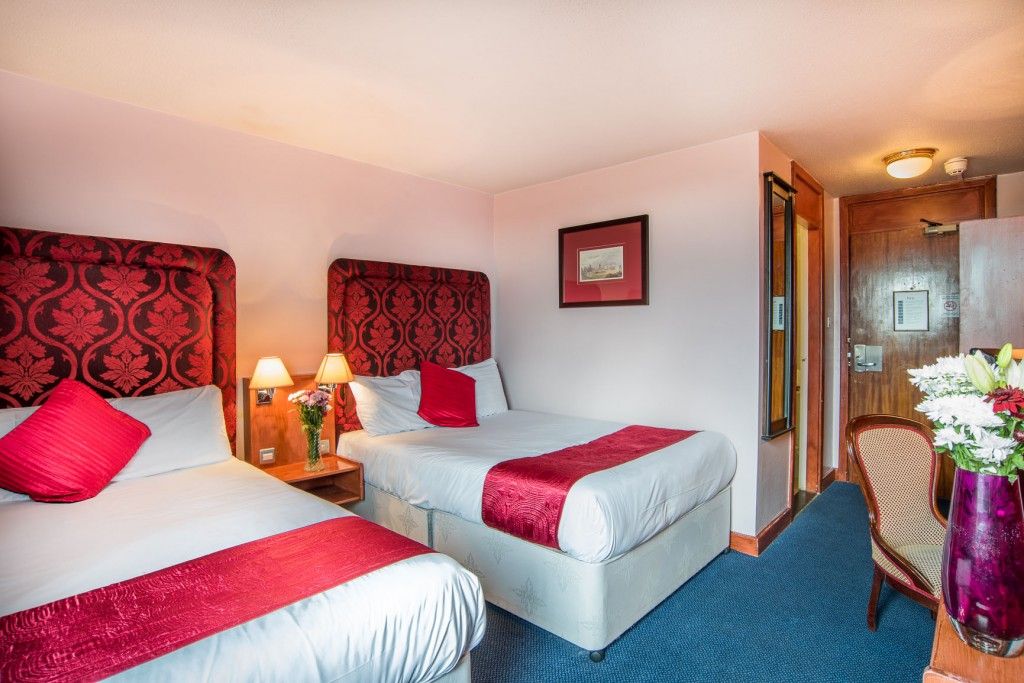 A hotel room with two beds, a nightstand with lamps, a framed picture on the wall, and a wooden door.