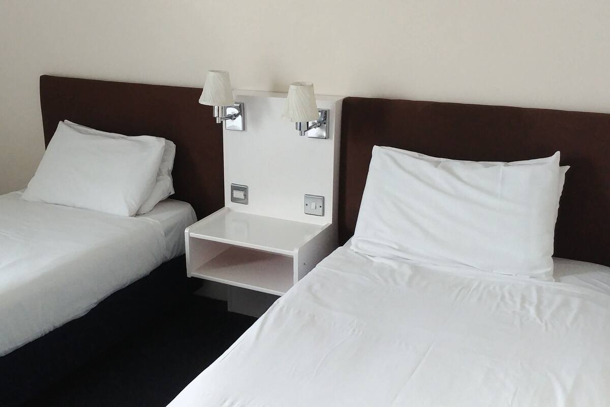 Two single beds with white linens and a nightstand between them.