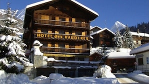 Ein mehrstöckiges Holzgebäude mit Balkonen, mit der Aufschrift "HOTEL des HAUDERES", umgeben von schneebedeckten Bäumen und Bergen.