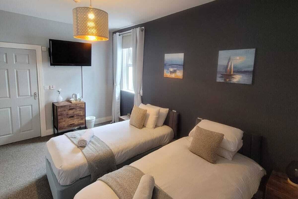 A hotel room with two beds, a TV, a painting, and a lamp.