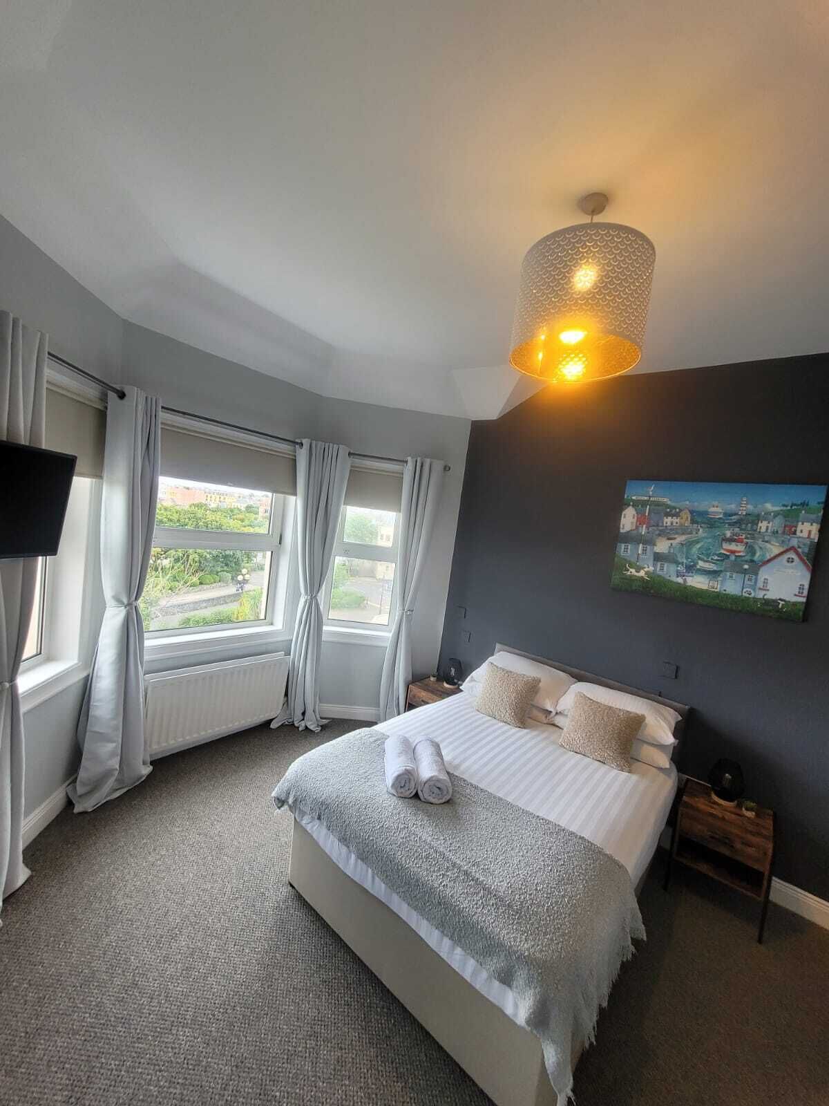 A bedroom with a large bed, a painting on the wall, and a window with curtains.