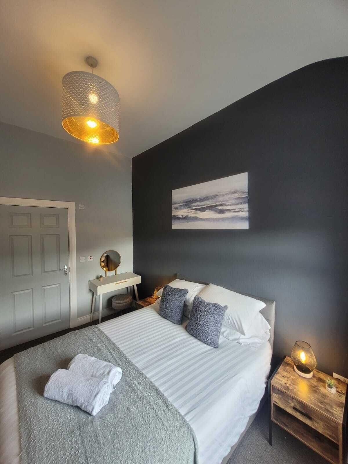 A bedroom with a bed, bedside table, lamp, and a painting on the wall.
