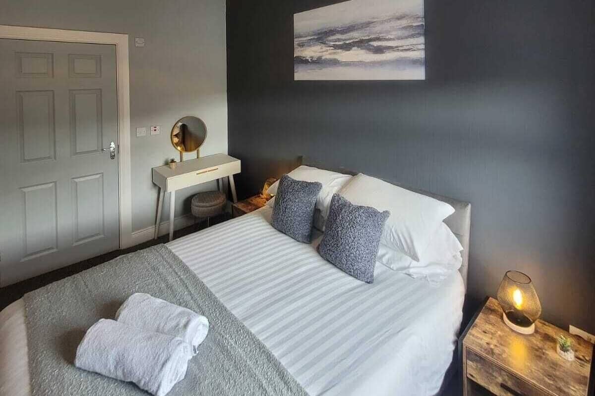 A bedroom with a bed, bedside table, lamp, and a painting on the wall.